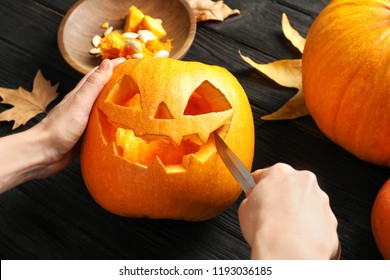 Woman carving Halloween pumpkin head jack lantern on wooden table, closeup
