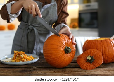 Woman carving pumpkin at table in kitchen. Halloween celebration