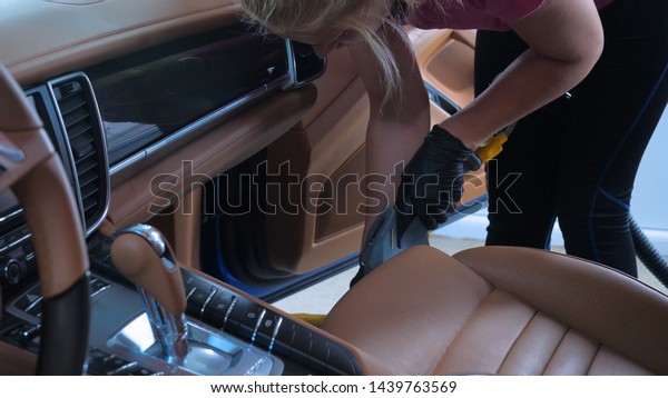 A woman at the carwash is\
doing a full dry cleaning using a vacuum cleaner and black gloves.\
Concept of: Full car cleaning, Dry cleaning, Professional\
service.
