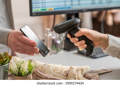 Woman Cashier Scanning Qr Code From Buyer Phone Using Barcode Scanner. Man Buying A Gift In A Female Clothing Store Using Promo Code.  