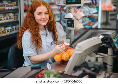 Woman cashier sitting behind checkout  and working in supermarket. Female checkout counter clerk scanning grocery products and looking at camera. - Powered by Shutterstock