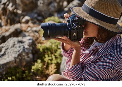 A woman in casual attire and a straw hat takes photographs in an outdoor natural setting. Captures the essence of outdoor photography and creativity. - Powered by Shutterstock