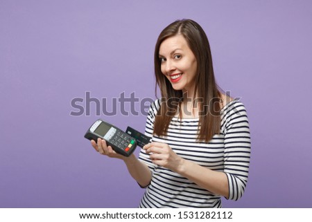 Woman in casual clothes isolated on violet background studio portrait. People lifestyle concept. Mock up copy space. Hold wireless modern bank payment terminal to process acquire credit card payments