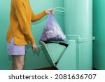 A woman in casual clothes throws a bag of garbage into the garbage chute