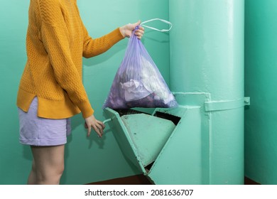 A woman in casual clothes throws a bag of garbage into the garbage chute