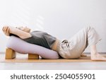 Woman in casual clothing doing yin,restorative yoga with bolster supported by blocks