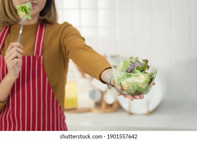 Woman In Casual Outfit Wearing Apron Eating Healthy Salad Anmd Give To Someone Concept In Modern Kitchen Room