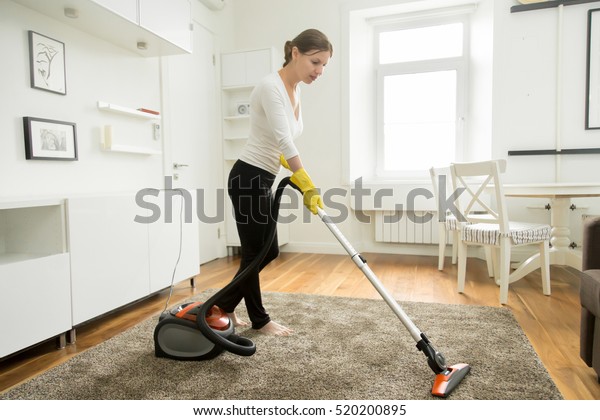 Woman in casual\
wear vacuum cleaning the carpet, tidying white modern living room.\
Home, housekeeping concept\
