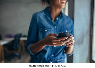 Woman in casuals standing in office by a window with phone in hand. Businesswoman with mobile phone in hand. - Powered by Shutterstock