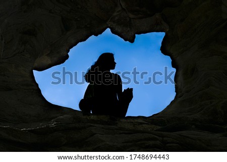 Woman Caver Spelunker exploring inside of a Dark Cave. female sitting at the edge of the cave hole. Oval shaped of cave hole.Silhouette of a girl standing in front of the entrance to the cave. Freedom