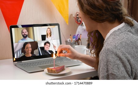 Woman celebrating her birthday through video call virtual party with friends. Lits and blows out candle. Authentic decorated home workplace. Coronavirus outbreak 2020.