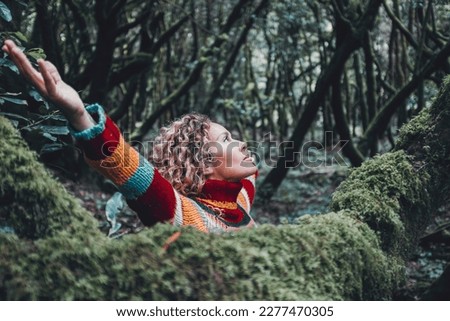 Woman celebrating nature lifestyle and outdoor leisure activity alone opening arms outstretching and looking the trees in forest green woods outdoor. Inner life balance mindful lifestyle female people