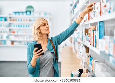 Woman with cell phone choosing vitamins from shelf in drugstore. - Powered by Shutterstock