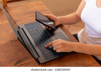 Woman With Cellphone In Hand And Typing On Laptop. Home Office