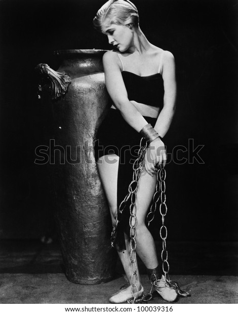 Woman chained in front of\
a big vase