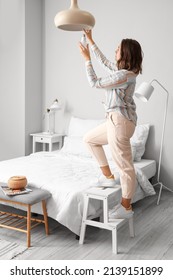 Woman Changing Light Bulb In Hanging Lamp At Home