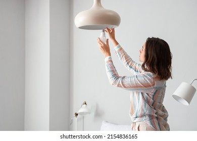 Woman changing light bulb in hanging lamp at home