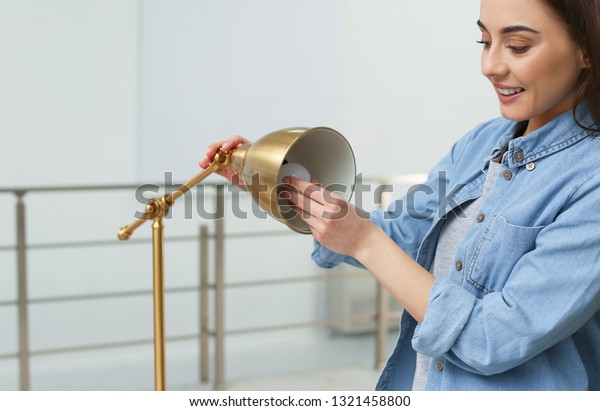 Woman changing light\
bulb in lamp indoors