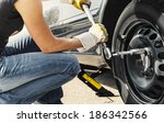 Woman is changing  tire of her car with wheel wrench.