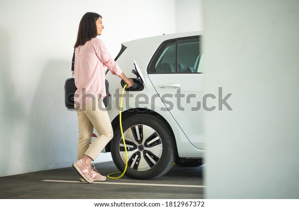 Woman charging a\
electric car at a garage
