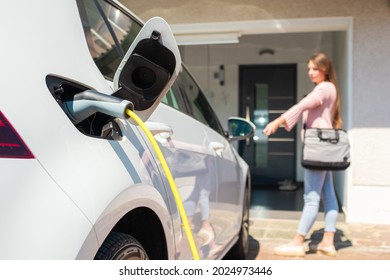 Woman Charging Electric Car At Home With Cable.