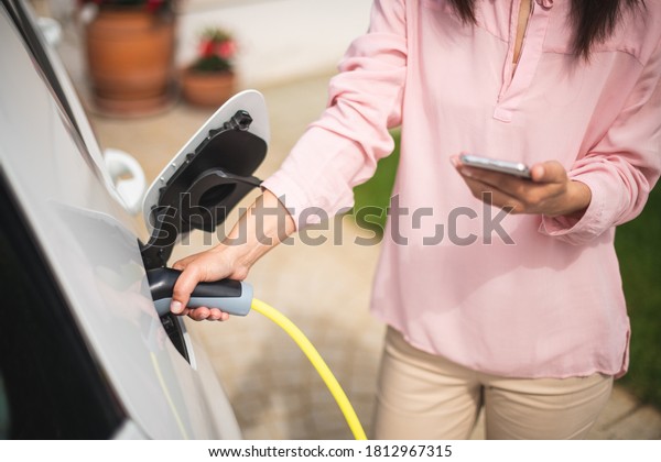 Woman charging electric car and making time\
adjustment on a\
smartphone