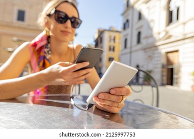 Woman Charging Phone With A Power Bank While Sitting At Cafe Outdoors. Concept Of Charging Gadgets For Travel