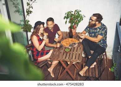 Woman In Checkered Dress And Hat Eating Pizza On Her Small Apartment Porch With Two Male Friends