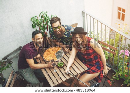 Woman in checkered dress takes photo with friends on patio while wearing black hat