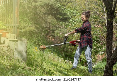 Woman In Checkered Shirt Mowing Grass With Electric Lawn Mower.