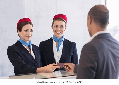 Woman In Checkin Counter Taking Passport For Verification From Passenger Man. Happy Smiling Hostess At Check In Working With Her Colleague. Businessman On A Business Trip In Airport.