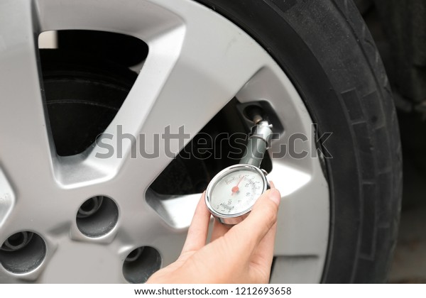 Woman\
checking car tire pressure with air gauge,\
closeup