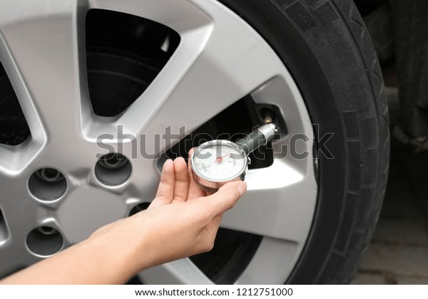 Woman
checking car tire pressure with air gauge,
closeup