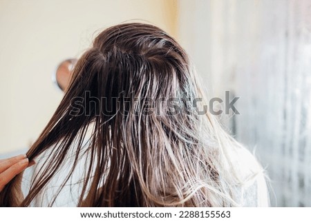 Woman checking dirty oily and greasy hair looking in mirror at home. Bad hair care cosmetics concept. Back view