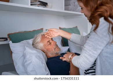 Woman checking fever temperature of senior man lying on bed. Old husband resting at home feeling sick while 
while his wife assists him. Feverish man feeling the seasonal symptoms of the flu.  - Powered by Shutterstock