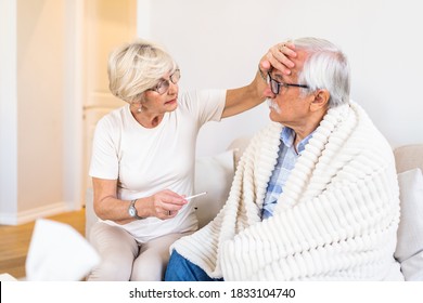 Woman Checking Fever Temperature Of Senior Man. Old Husband Resting At Home Feeling Sick While His Wife Checking Fever By Touching Forehead