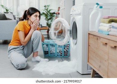 Woman checking her damaged washing machine, the floor is flooded - Shutterstock ID 2179959017