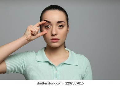 Woman checking her health condition on grey background. Yellow eyes as symptom of problems with liver - Shutterstock ID 2209859815