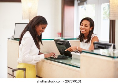 Woman Checking In At Hotel Reception Using Digital Tablet