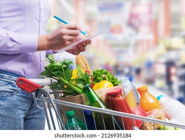 Woman checking a shopping list and buying goods at the supermarket, her shopping cart is full