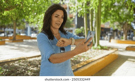 Woman checking smartwatch while taking selfie in urban park, showcasing technology use among mature individuals in outdoor city setting - Powered by Shutterstock