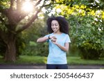 Woman checks her smartwatch in a sunny park, embracing fitness and relaxation through outdoor activity and positive energy.