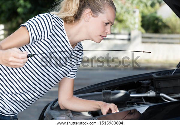 woman checks the oil in\
the cars engine