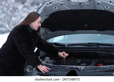 Woman checks the oil in the engine of the car in winter weather. Preparing the car for winter driving