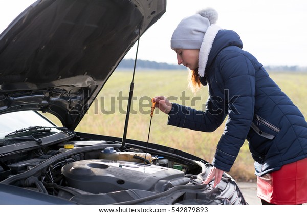 woman checks the oil level in the engine. Damage to\
the vehicle on the road