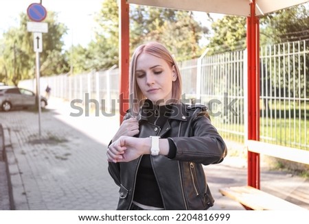 a woman checks the time at a bus stop while waiting for a bus, tram, trolleybus. Riding on public transport to work, study, university. Late. Route schedule.