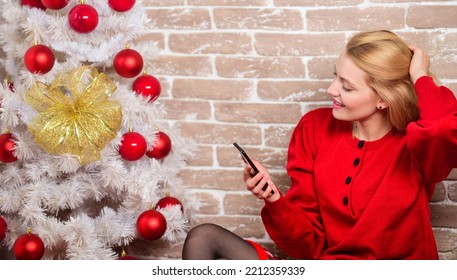 Woman Cheerful Hold Smartphone Enjoy Mobile Phone Conversation. Girl In Dress Sit Near Christmas Tree With Ornaments. Wishing Everyone Merry Christmas. Waiting For Christmas. Voicemail Greeting