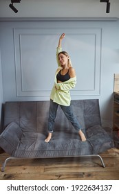 Woman In A Cheerful Mood Lifting Right Hand While Staying Barefoot On Grey Couch