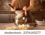 woman chef in brown apron sifts flour through sieve for making dough on kitchen background