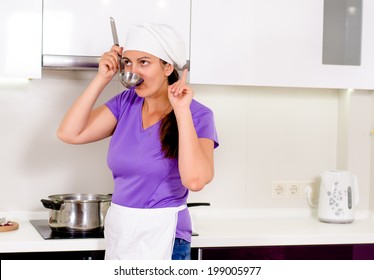 Woman Chef Having A Brainwave As She Tastes The Food In The Saucepan From A Ladle Raising Her Finger As She Thinks Of A New Or Missing Ingredient